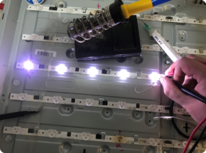 Technician testing LED backlight strips inside a television during repair